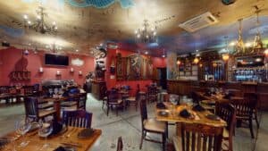 The dining room at Jack's Steak House with red walls, iron chandeliers and the bar along the far side