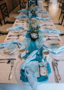 A long banquet table set for an event at Jazmin's Restaurant, with light-blue napkins, glassware and baby's breath centerpieces