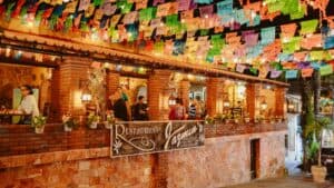 Diners on the brick terrace of Jazmin's Restaurant at night, under strings of papel picado and lanterns, above the Restaurant Jazmin's sign