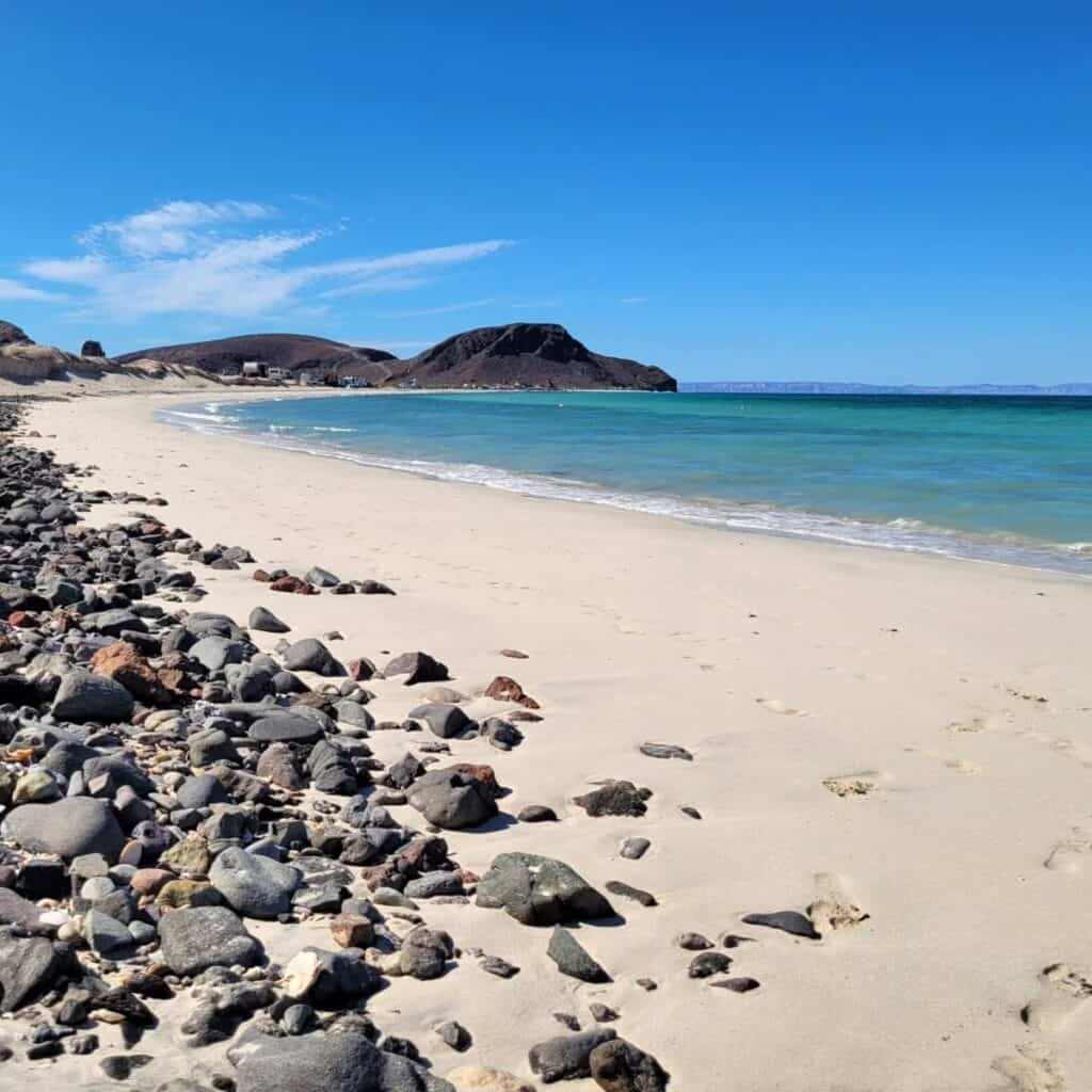 Pebbles and pale sand at Playa El Tecolote with the headland behind