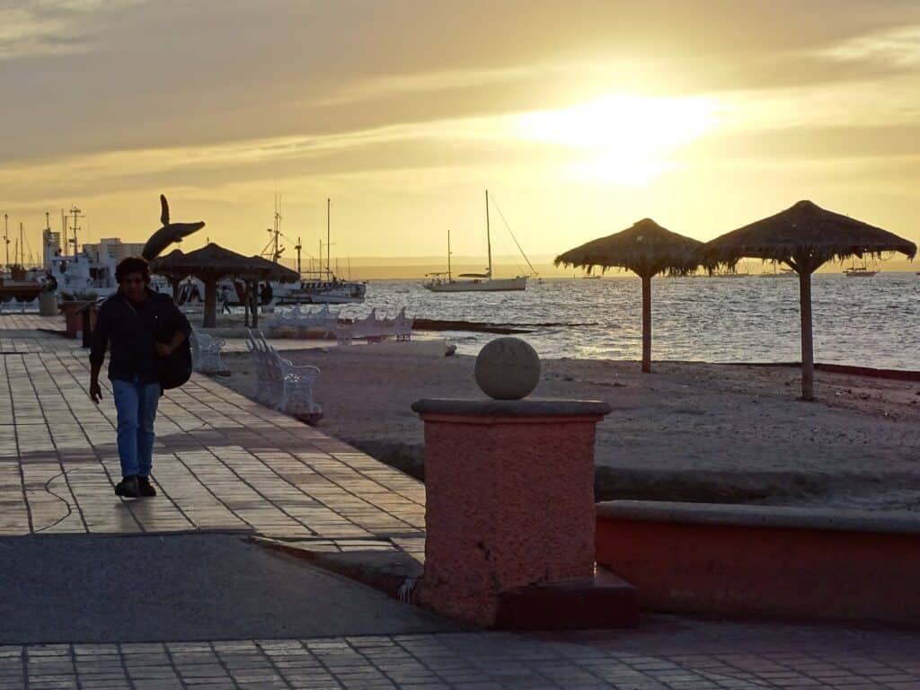 Sunset on the malecón of La Paz, with palapas and the whale-tail sculpture in silhouette