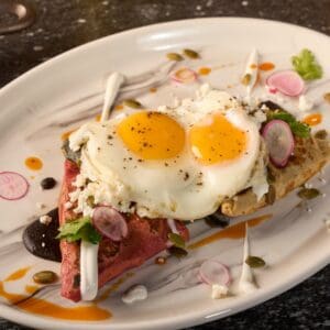 Two fried eggs over folded red and green tortillas with fresh cheese, radish and pumpkin seeds, a breakfast plate at Los Deseos