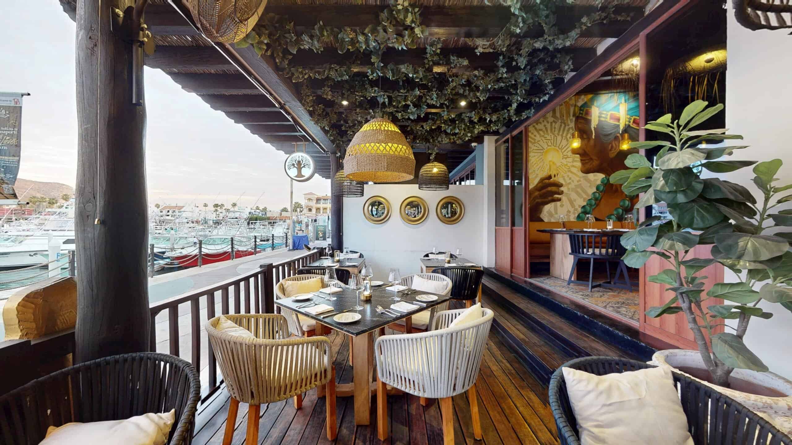 The covered terrace at Los Deseos, with rattan lamps and set tables beside the yachts of the Cabo San Lucas marina