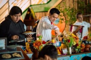 A cook in a white jacket serving from clay and enamel pots at the buffet station at Mango Deck, decorated with marigolds