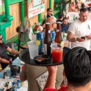 A server carrying a tray of beers, a michelada and a bowl of salsa through the dining area at Mango Deck