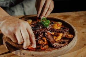 Chef Ubaldo Martínez finishing a course of grilled octopus with cherry tomatoes on a wooden board at Monte Cardón