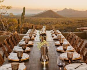 A long table with amber glassware on the terrace at Monte Cardón, with cardón cactus and desert hills in the evening light