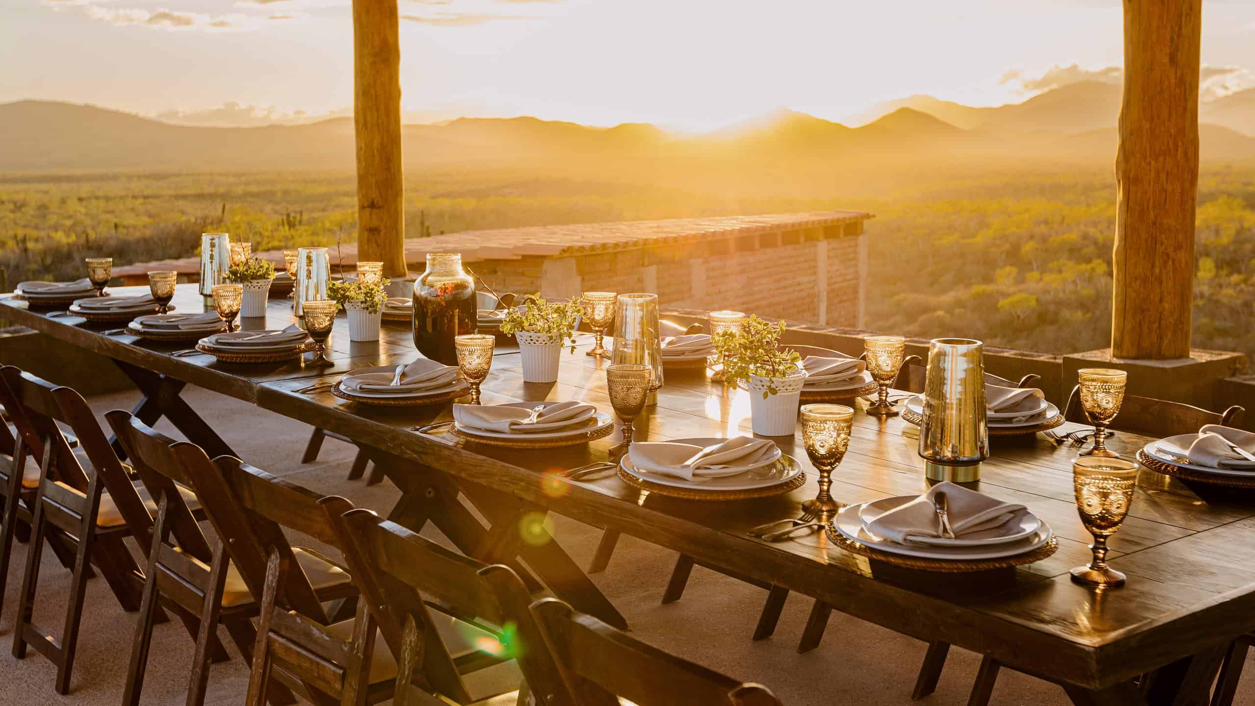 A long dinner table set on the covered terrace at Monte Cardón as the sun goes down over the desert and the mountains
