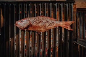 A whole scored red fish grilling over the open wood fire in the kitchen at Monte Cardón
