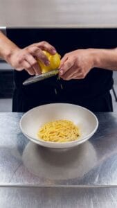 A cook grating lemon zest over a bowl of pasta at Mozza Baja