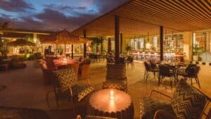 The open-air terrace at Mozza Baja at dusk, with lounge chairs, candlelit tables and the bar under a slatted wood roof in the Costa Palmas Marina Village