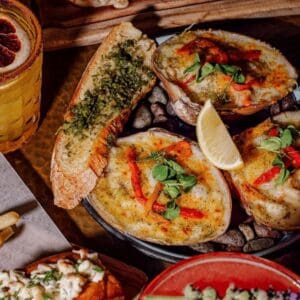 Baked oysters topped with red pepper and microgreens, with grilled bread and lemon, at Oystera