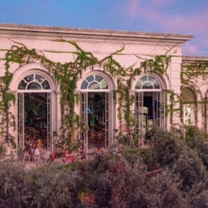 The front of the building that houses Oystera, with tall arched windows and climbing vines, seen from the garden at dusk