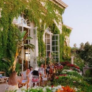 Guests dining among flower beds in front of the vine-covered building at Oystera