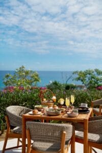 A breakfast table on the Palmerio terrace with pastries, fruit and juice, above the gardens and the ocean