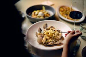 A bowl of pasta with clams at a dinner table at Palmerio, next to a glass of red wine