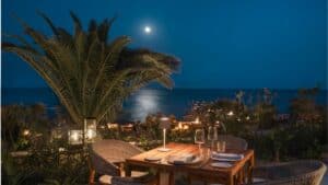 Terrace tables at Palmerio at night, lit by small lamps, with palms and moonlight on the ocean