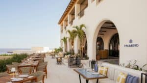 The open-air terrace at Palmerio, with set tables along the white arched facade and the ocean in the distance