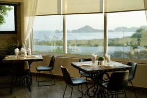 Set tables in the Puerta Vieja dining room by tall windows that look across the bay to the Arch of Cabo San Lucas