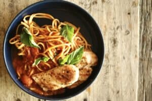 Spaghetti pomodoro with grilled chicken breast and fresh basil in a dark bowl at Puerta Vieja