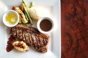 A grilled steak with a lobster tail, grilled vegetables, mashed potato, drawn butter and sauce at Puerta Vieja