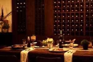 A table set with dinner plates, wine and cocktails in front of the wine cellar wall at Puerta Vieja
