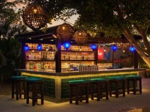 The outdoor bar at Talay at night, with woven lanterns, blue glass lights and stools along a green-tiled counter