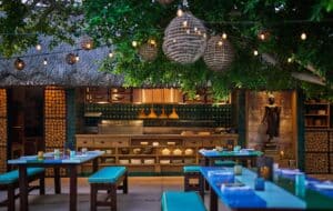 The open kitchen at Talay under its palm-frond roof, with a Buddha statue beside it and set tables in front