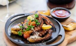 Grilled octopus with lemon, cherry tomatoes and grated cheese in a cast-iron pan at The Woods Cabo