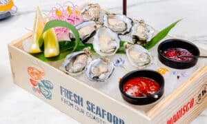 Fresh oysters on ice in a wooden seafood crate with mignonette and cocktail sauce at The Woods Cabo