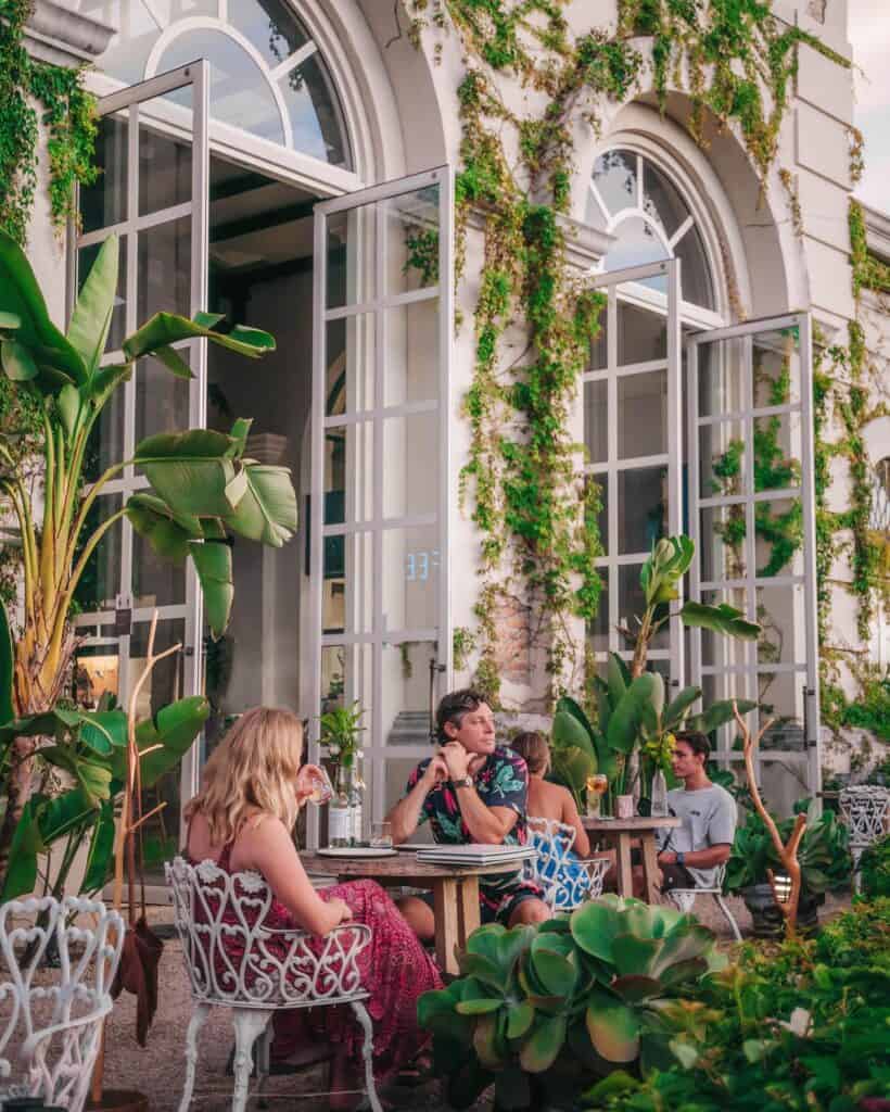 Guests at tables among plants outside the tall windows of Oystera in Todos Santos