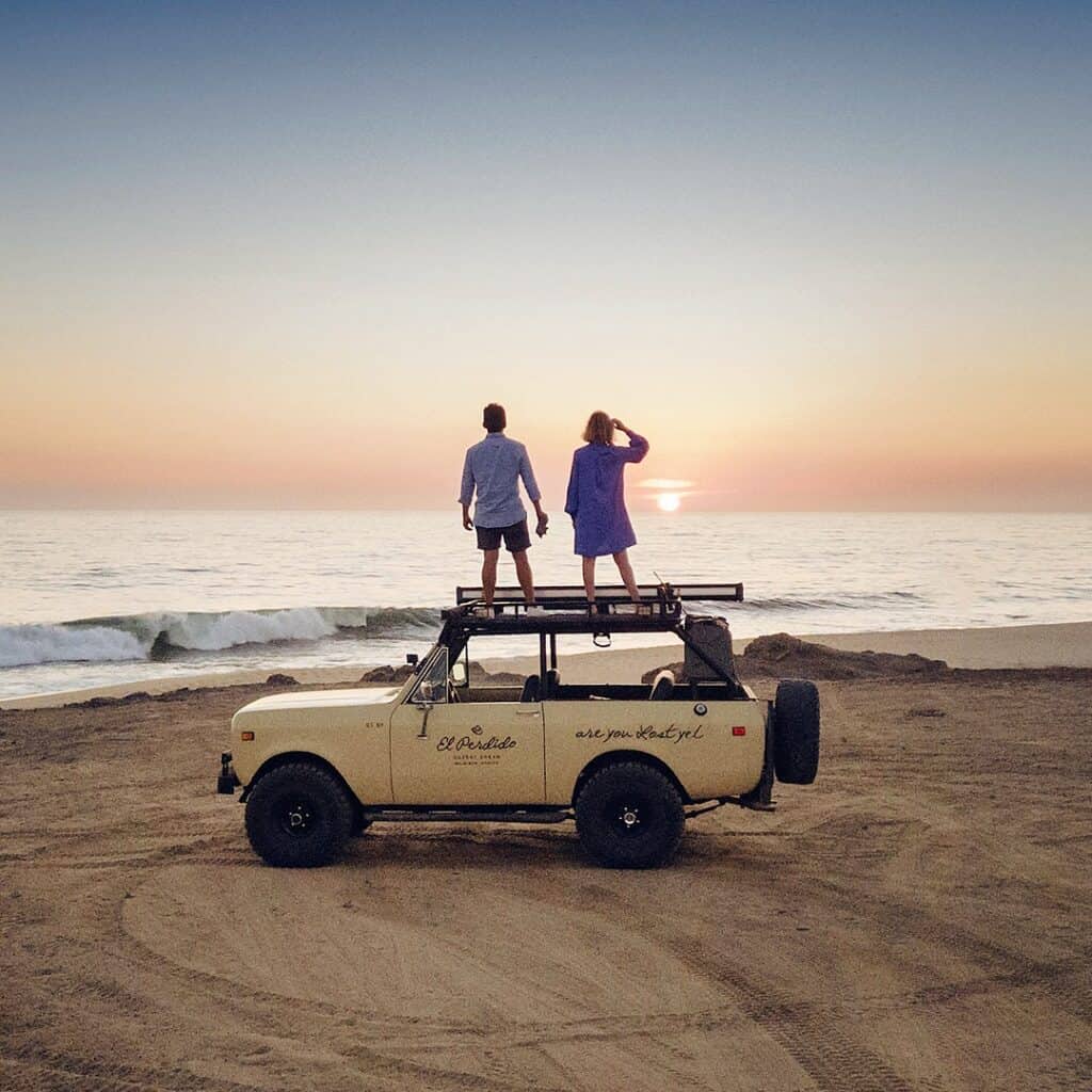 A couple on the roof of a vintage 4x4 watching the sunset at Playa Los Cerritos