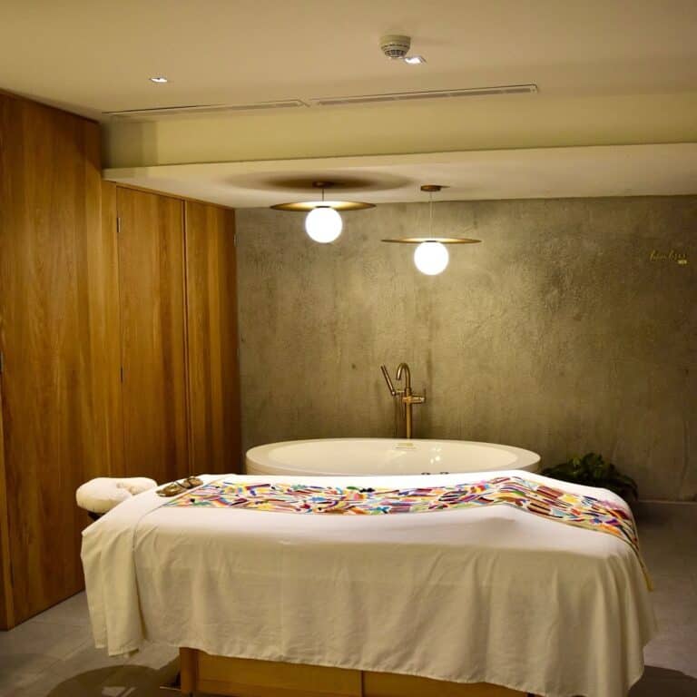 Massage table with an embroidered Mexican runner in front of a soaking tub at Amura Spa