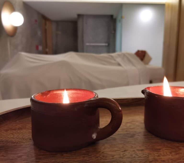 Lit massage candles in clay cups with a treatment table behind them at Amura Spa