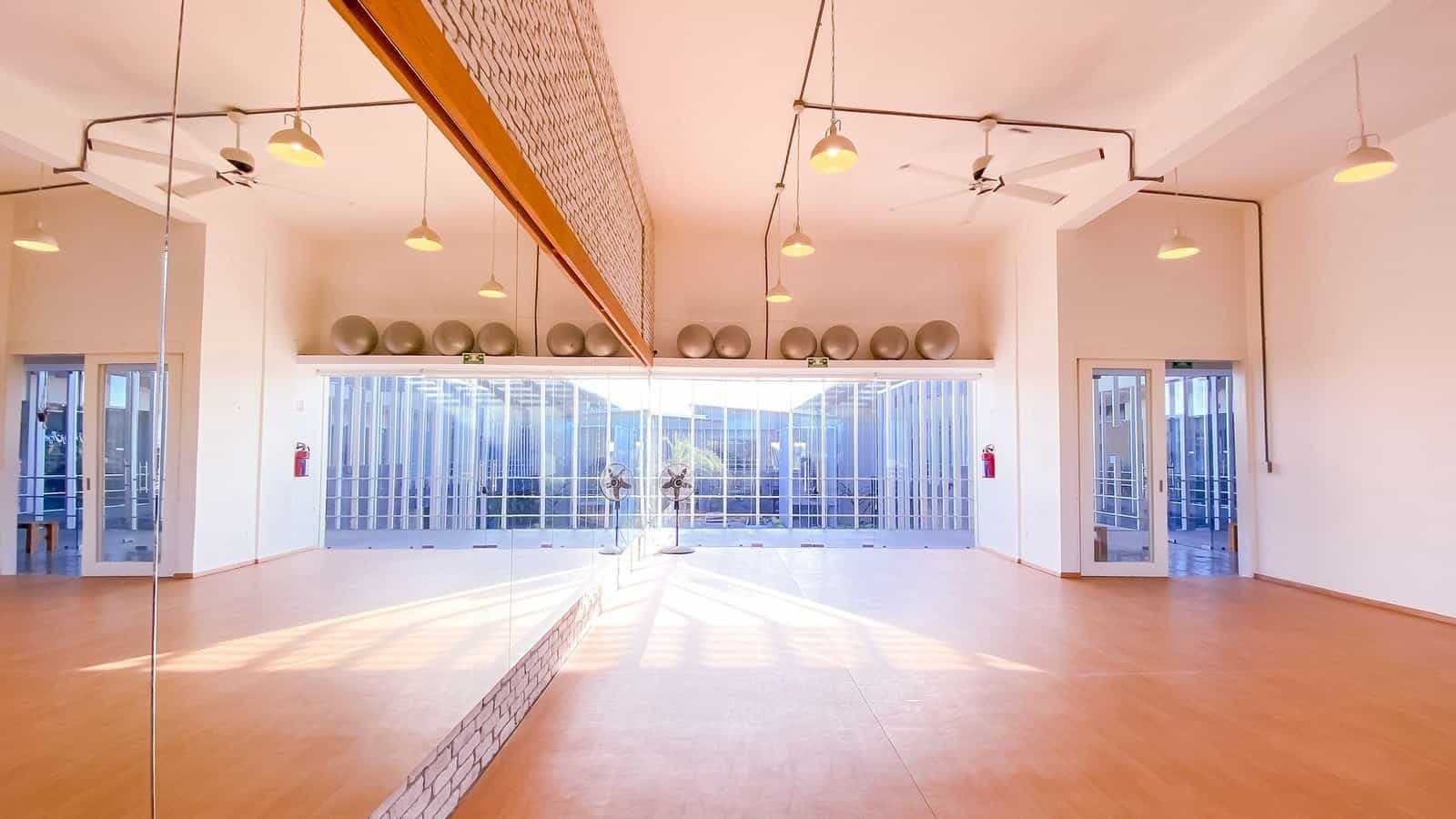 Empty studio at Cabo Yoga and Fitness with wood floors, a mirror wall, pendant lights and exercise balls