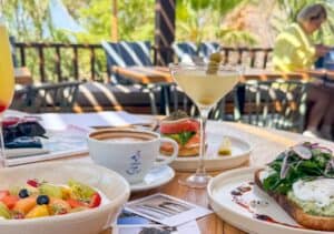 Avocado toast, a fruit bowl, a smoked salmon bagel and a martini on a table on the rooftop terrace of Cream Ánima Village