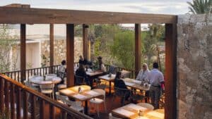 Diners at tables on the rooftop terrace of Cream Ánima Village in Cabo del Sol, under a wooden pergola in the late afternoon
