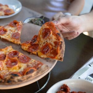 A hand lifting a slice of pepperoni pizza from a pie on a raised stand at Cream