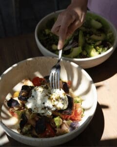 Two salad bowls with tomato, avocado, fresh cheese and pistachios on a sunlit table at Cream Ánima Village