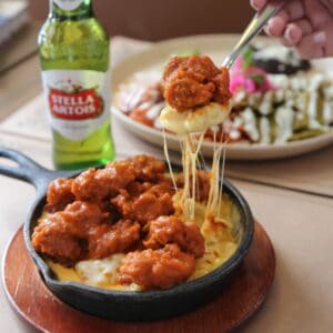 Boneless buffalo chicken over mac and cheese in a cast-iron skillet at Cream, with a beer on the side