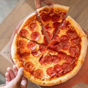 A whole pepperoni pizza cut into slices on a wooden peel at Cream