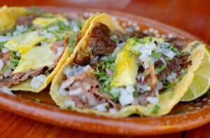 Three tacos with pineapple, onion and cilantro on a clay plate at Las Guacamayas