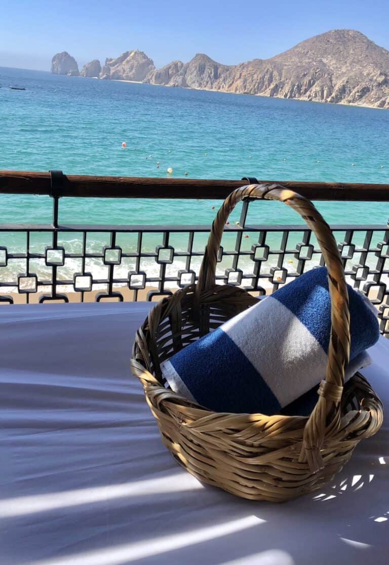 Rolled beach towel in a wicker basket on a massage table, with Land's End across the bay