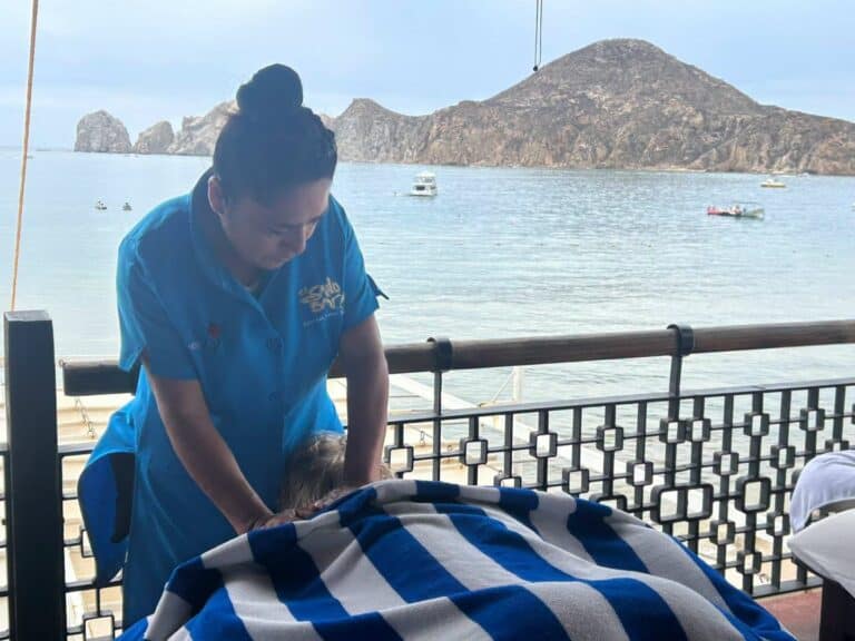 Therapist massaging a guest's back on the open-air deck, with Land's End behind