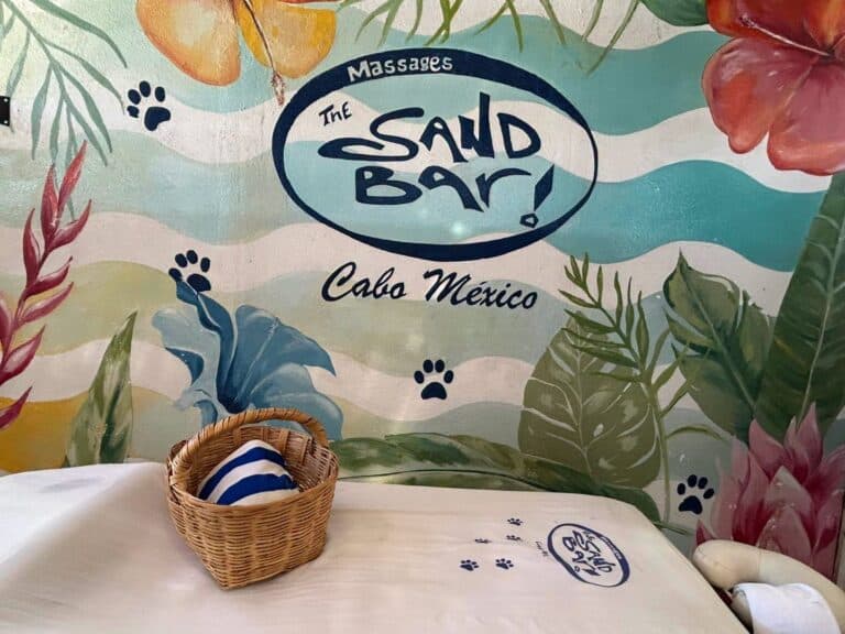 Massage table with a towel basket in front of the painted Massages at The Sand Bar mural