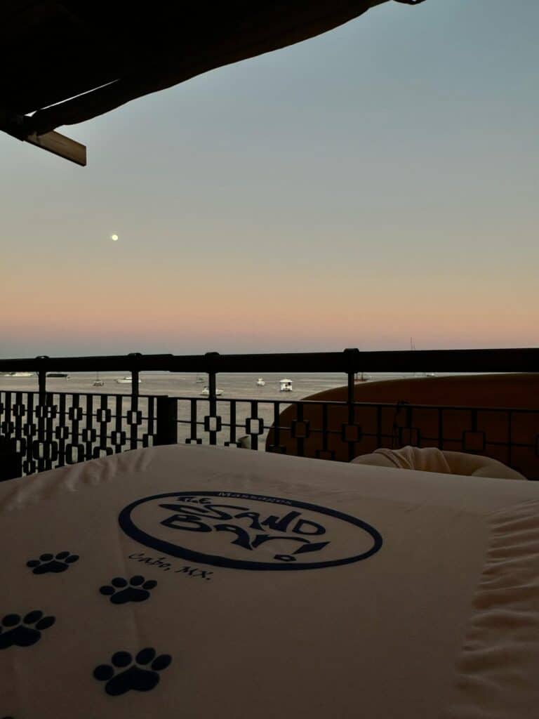 Massage table with The Sand Bar logo on the deck at dusk, with the moon over the bay
