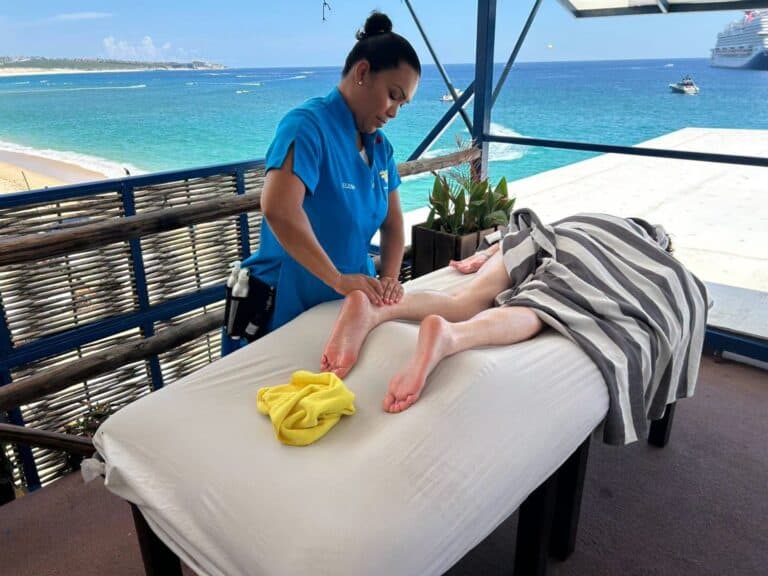 Therapist massaging a guest's legs on the deck overlooking Médano Beach and the bay