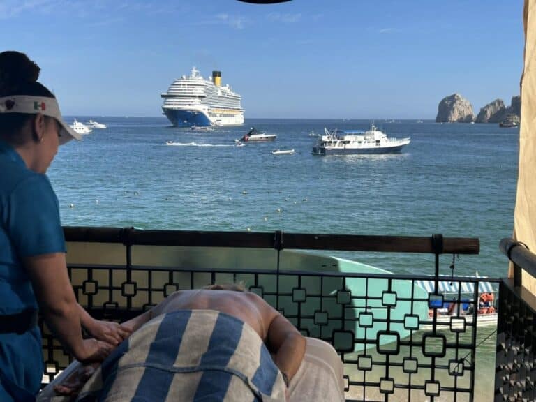 Guest receiving a back massage on the deck, with a cruise ship and the Arch in the bay