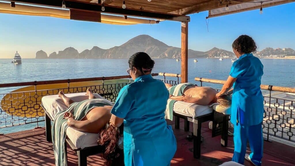 Two therapists giving massages on The Sand Bar's open-air deck, with Land's End across the bay