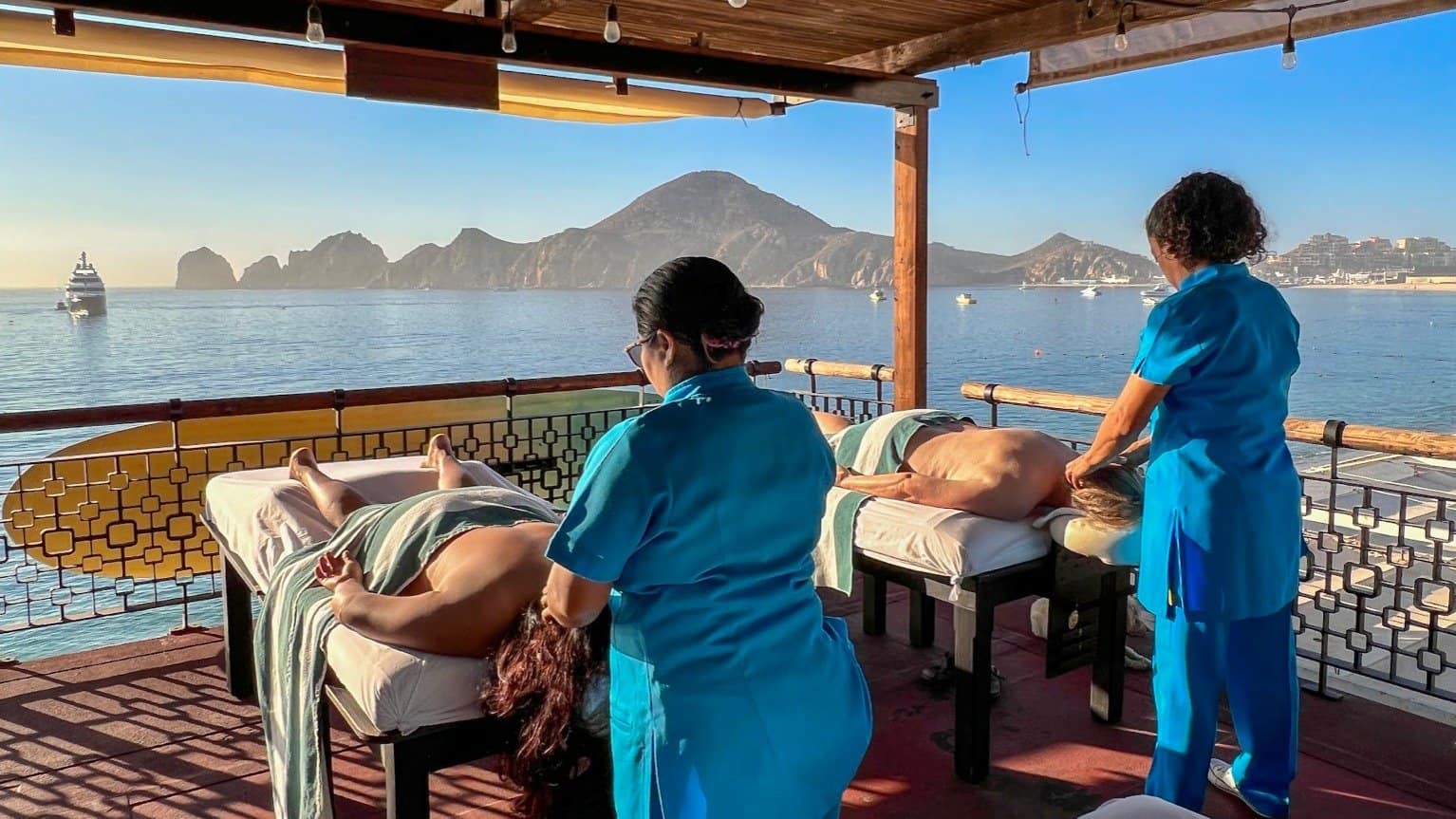 Two therapists giving massages on The Sand Bar's open-air deck, with Land's End across the bay